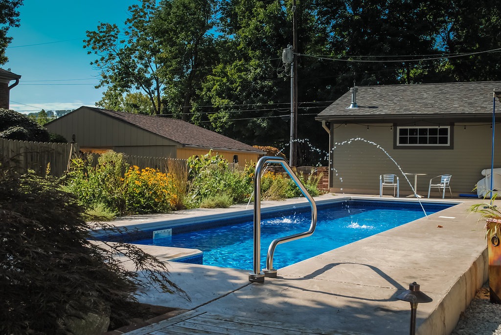 Backyard pool with garden and patio chairs.
