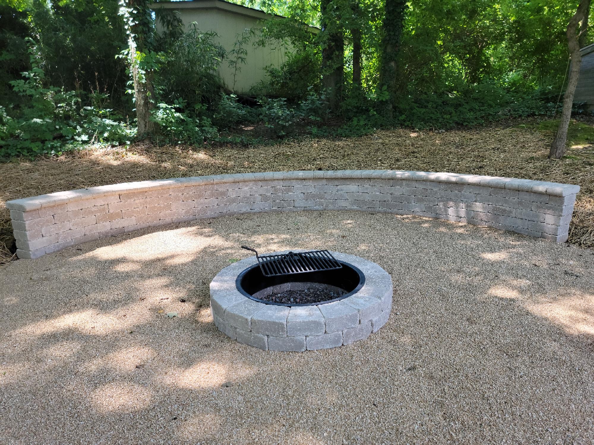 Outdoor fire pit with stone bench and grill.