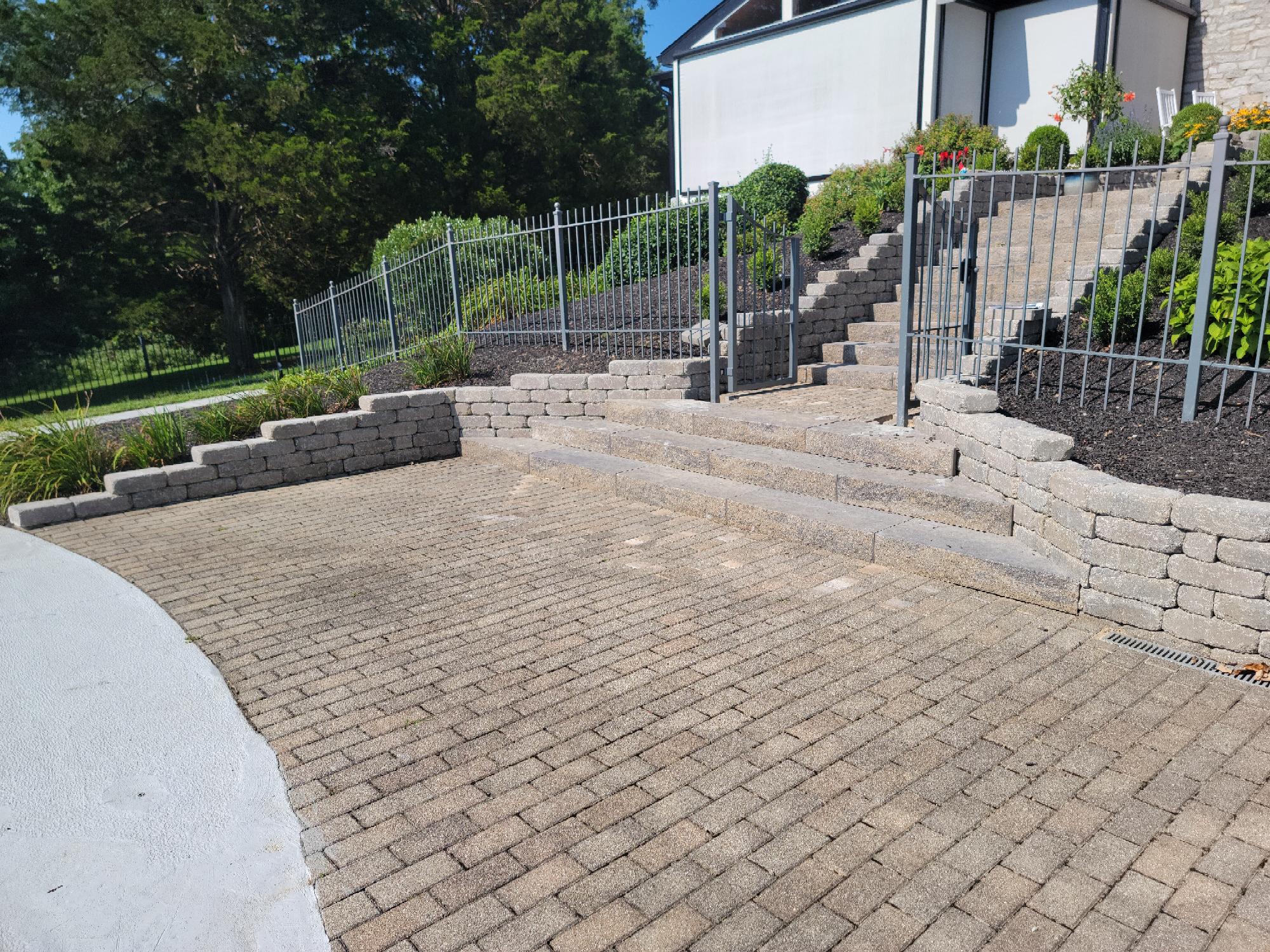 Brick patio with stone steps and metal fence.