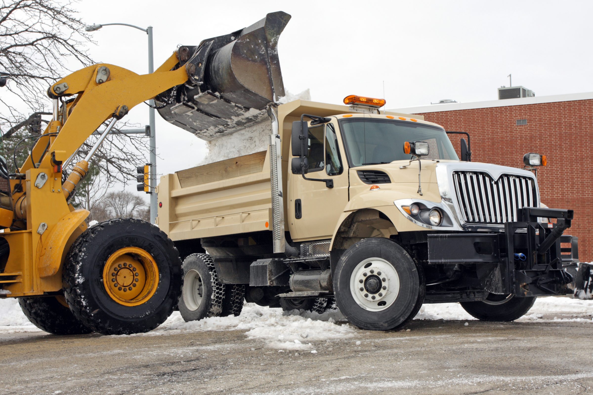 Bulldozer loading snow into dump truck in winter.