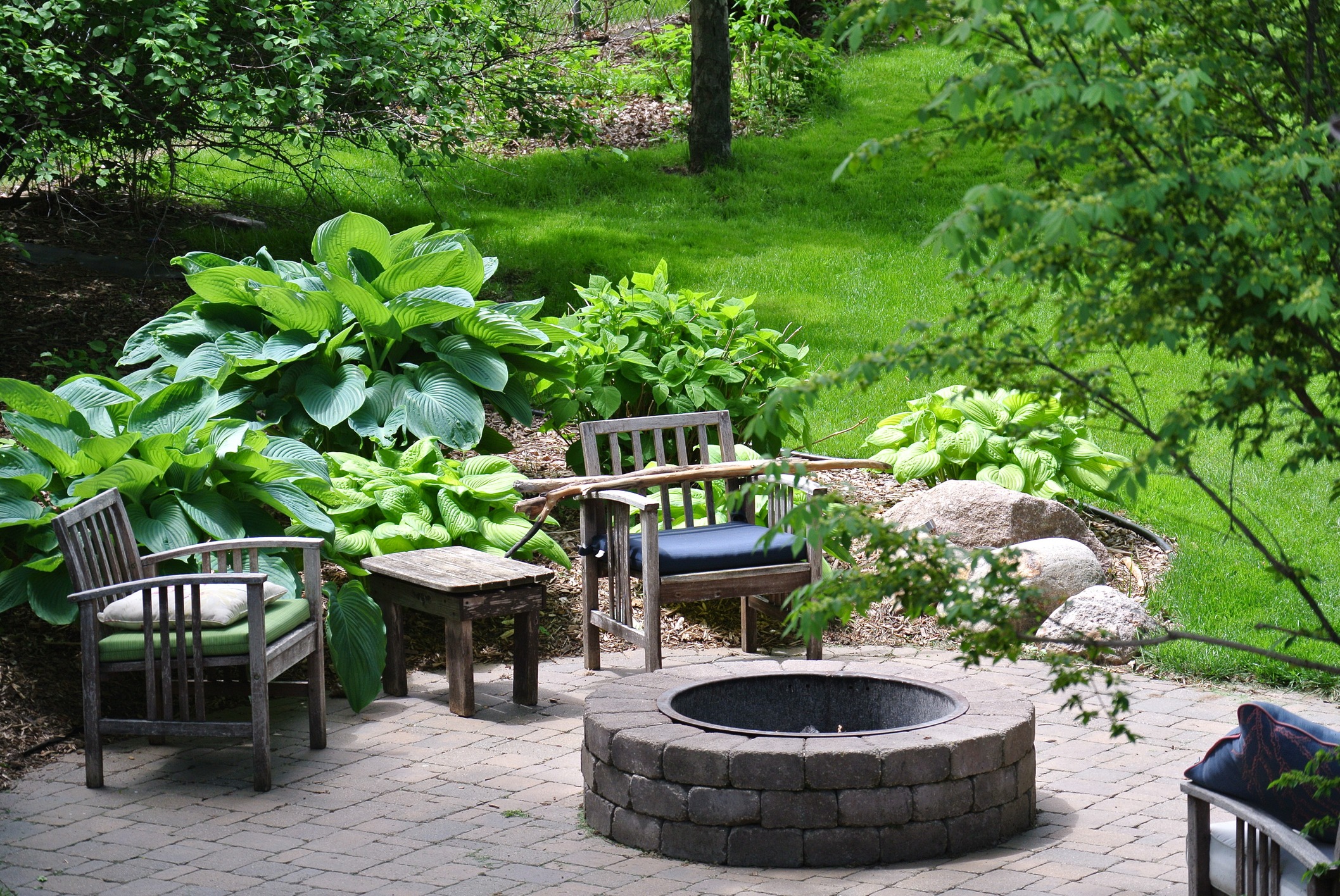 Backyard with chairs and fire pit surrounded by greenery.