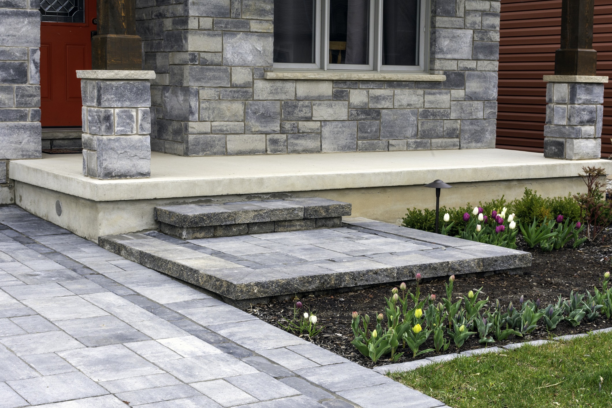 Stone porch with tulip garden and red door.