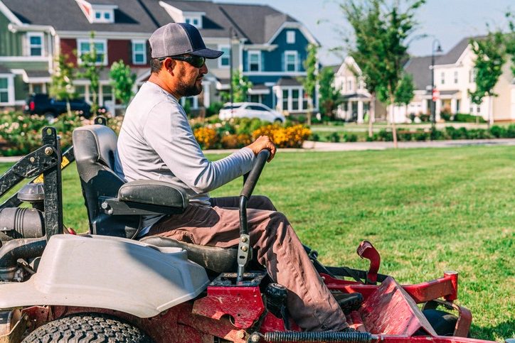 Man operating lawn mower in suburban neighborhood.