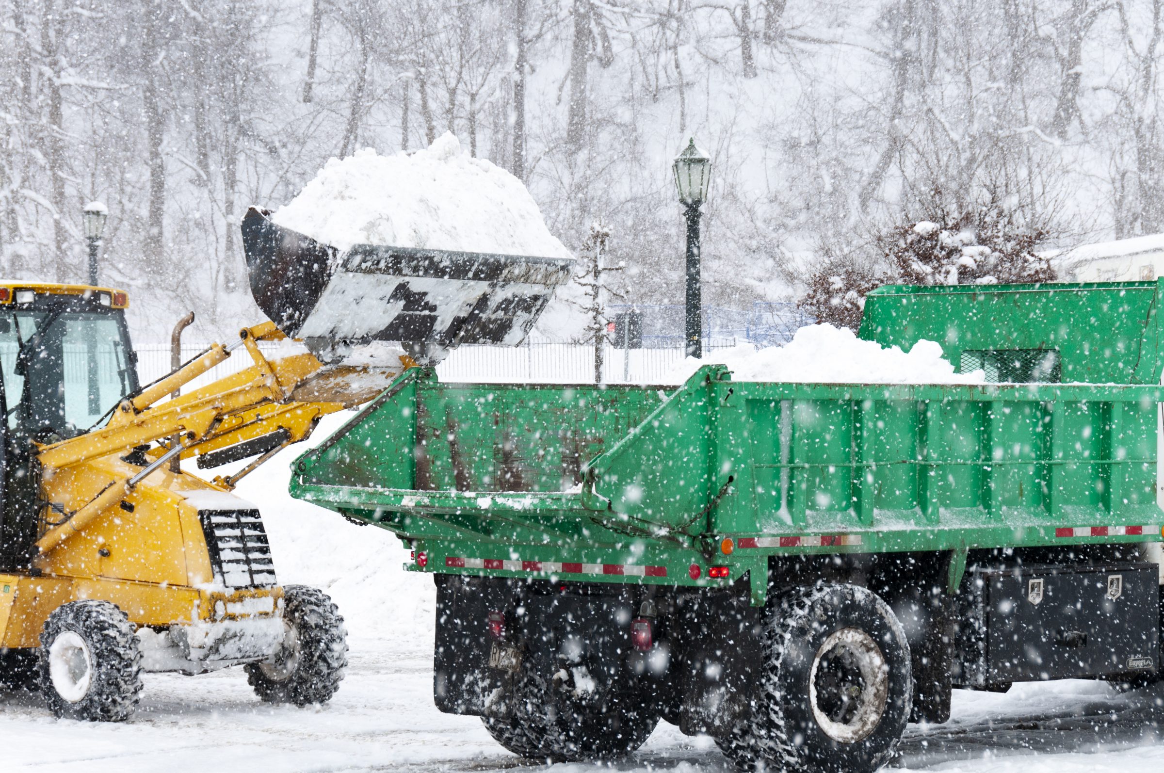 Loader dumping snow into truck during snowfall.