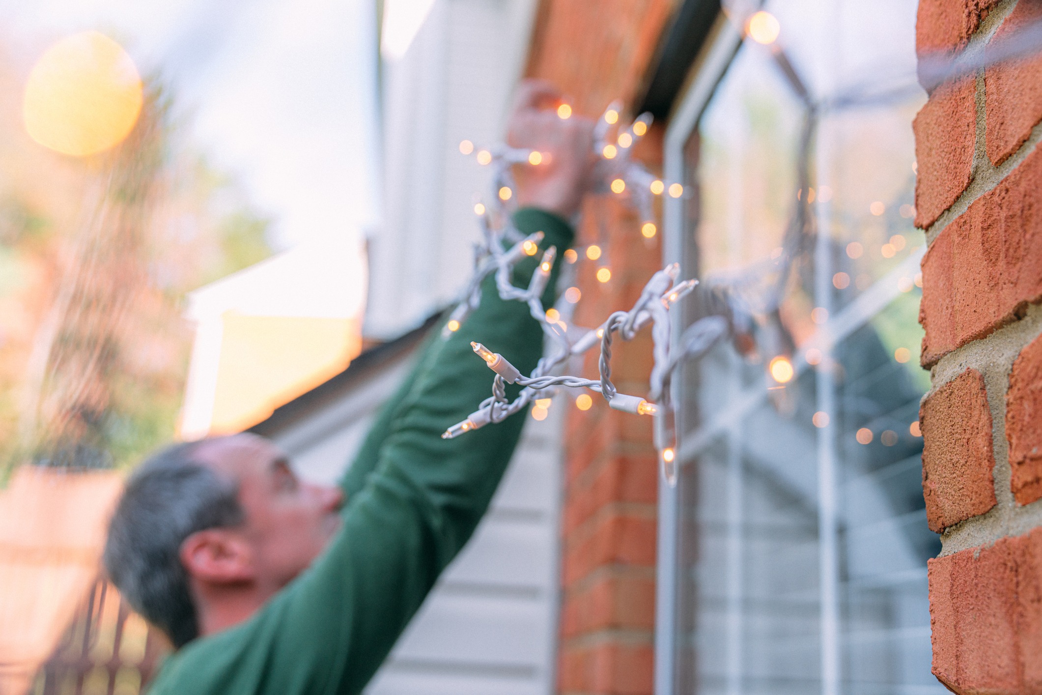 Person hanging outdoor string lights on house