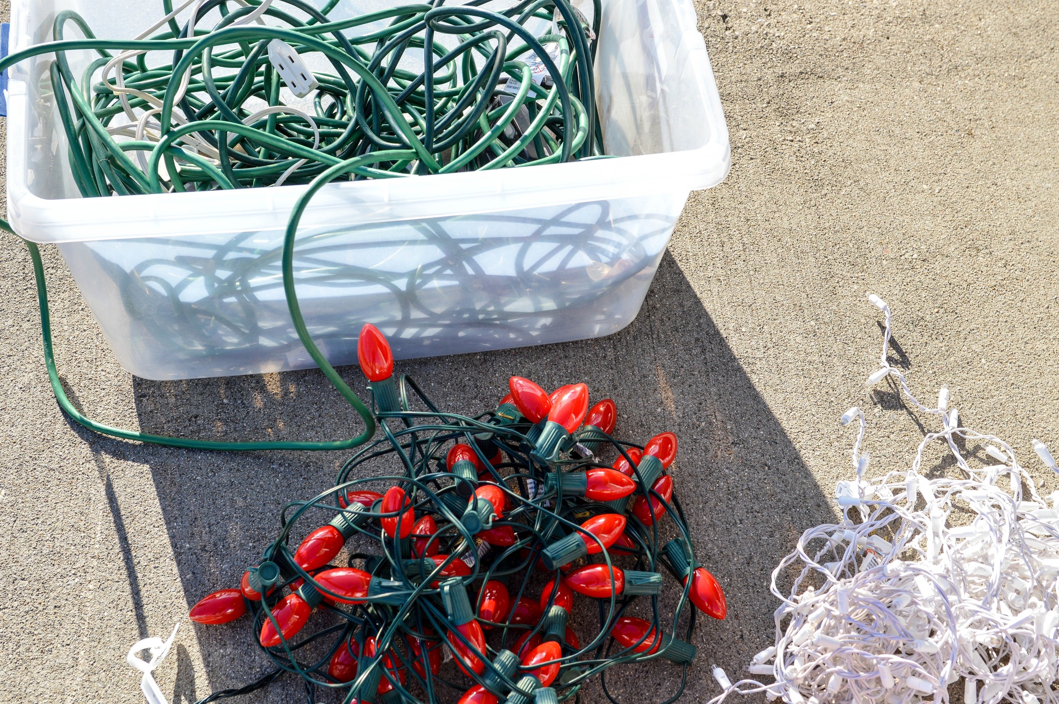 Box of tangled Christmas lights on concrete patio.
