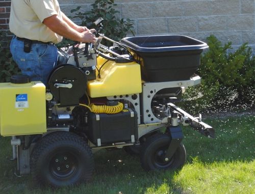 Person operating yellow lawn care equipment on grass.